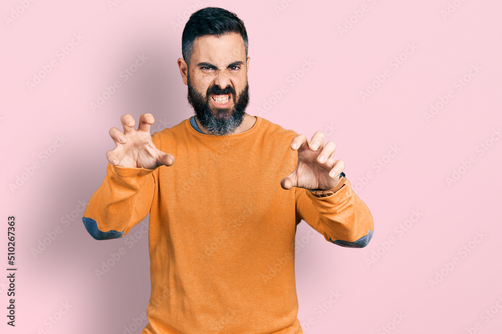 Hispanic man with beard wearing casual winter sweater smiling funny doing claw gesture as cat, aggressive and sexy expression Hispanic man with beard wearing casual winter sweater smiling funny doing claw gesture as cat, aggressive and sexy expression