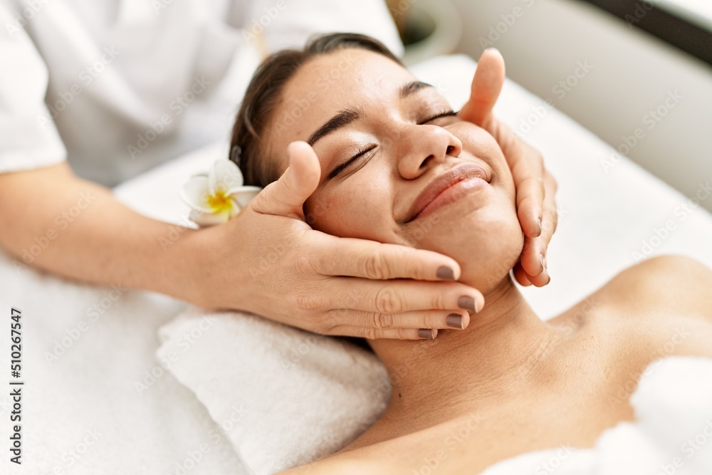 Young latin woman relaxed having face massage at beauty center Young latin woman relaxed having face massage at beauty center