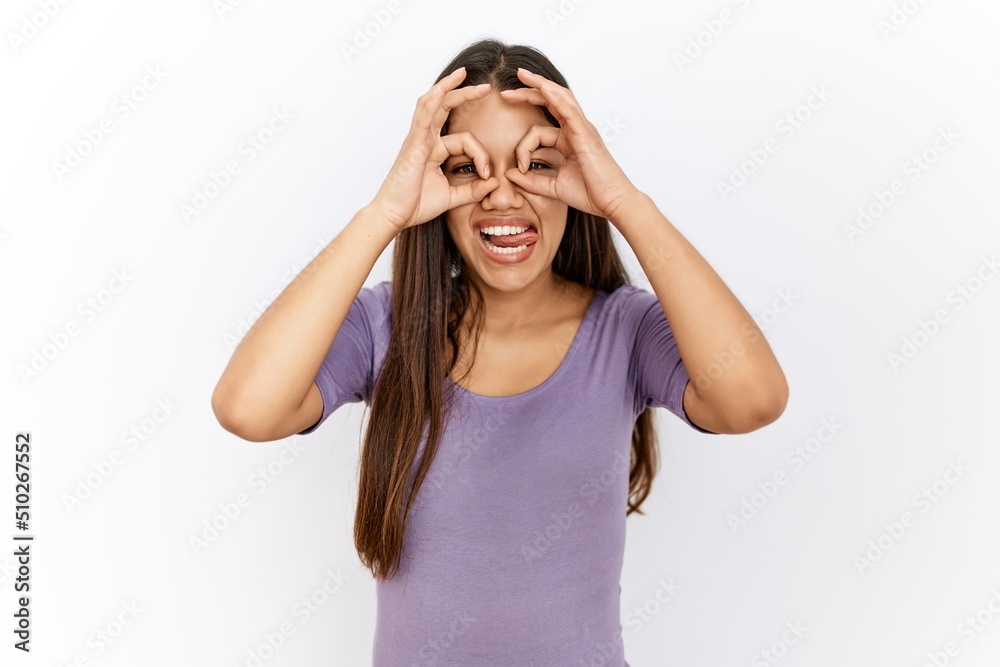 Young brunette woman standing by isolated background doing ok gesture like binoculars sticking tongue out, eyes looking through fingers. crazy expression. Young brunette woman standing by isolated background doing ok gesture like binoculars sticking tongue out, eyes looking through fingers. crazy expression.
