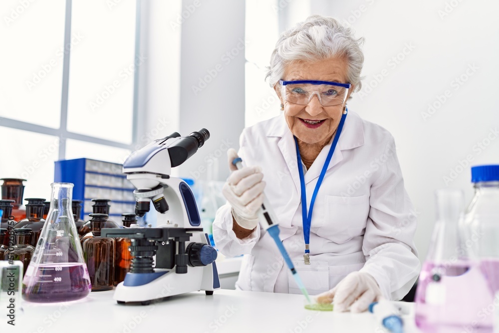 Senior grey-haired woman wearing scientist uniform using pipette at laboratory Senior grey-haired woman wearing scientist uniform using pipette at laboratory