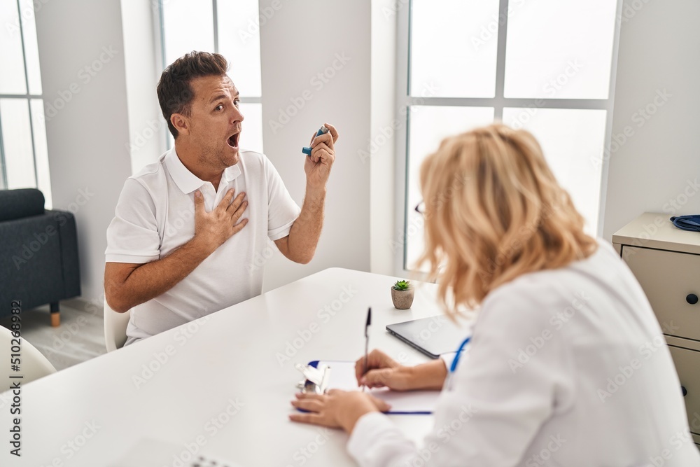 Obraz premium Middle age man and woman doctor and patient using inhaler having medical consultation at clinic