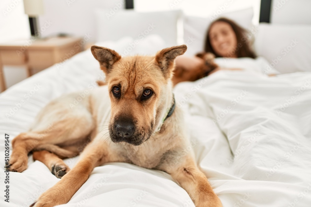 Young hispanic woman hugging dog lying on bed at bedroom