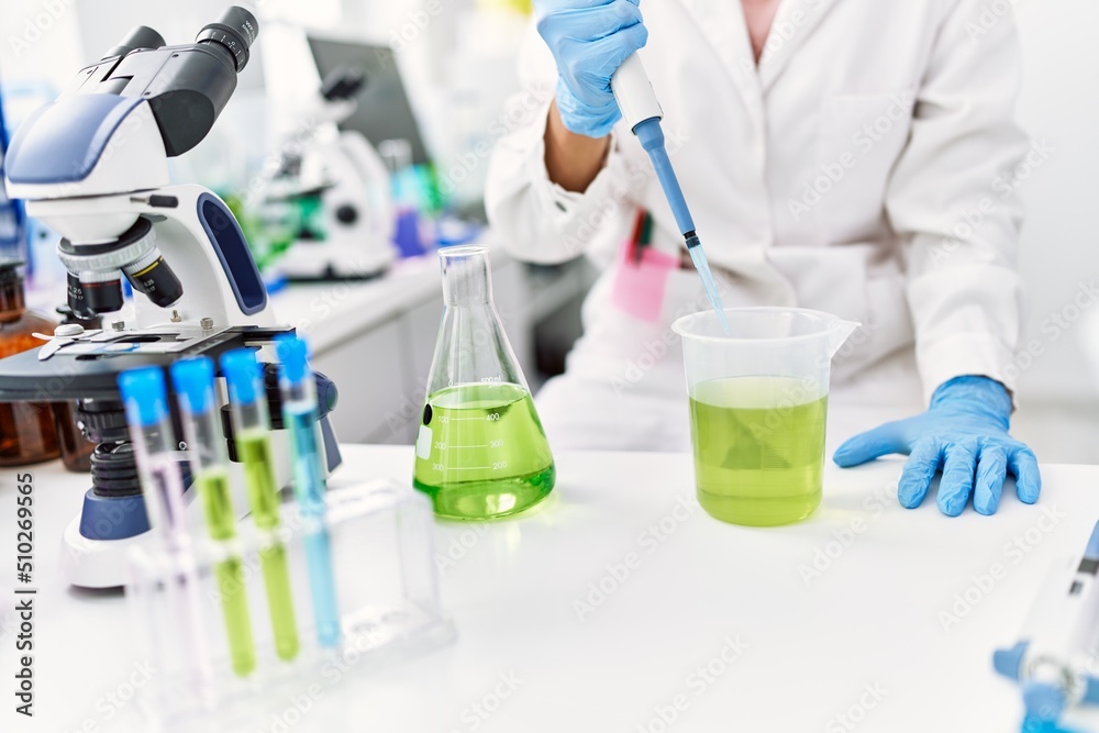 Young latin woman wearing scientist uniform pouring liquid on test tube at laboratory Young latin woman wearing scientist uniform pouring liquid on test tube at laboratory