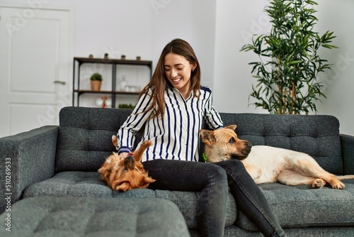 Sticker Young hispanic woman smiling confident sitting on sofa with dogs at home