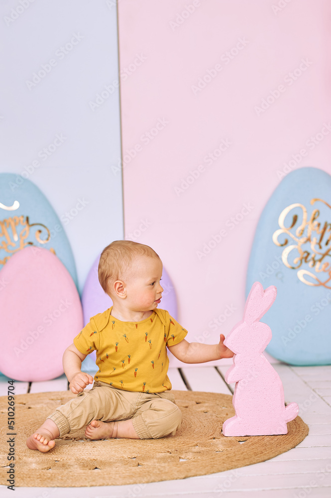 1 year old boy in yellow T-shirt, Easter decor, boy near two bunnies and large eggs