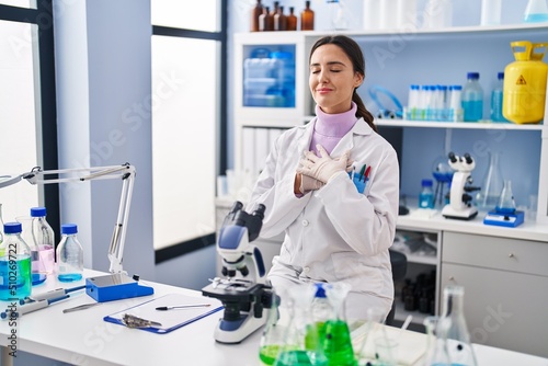 Young brunette woman working at scientist laboratory smiling with hands on chest with closed eyes and grateful gesture on face. health concept.