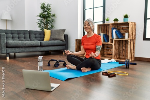 Middle age grey-haired woman smiling confident having online yoga class at home