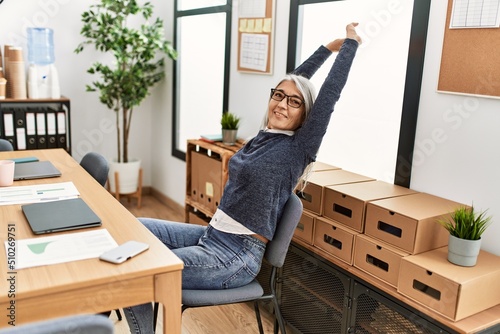Middle age grey-haired woman business worker stretching arms resting at office