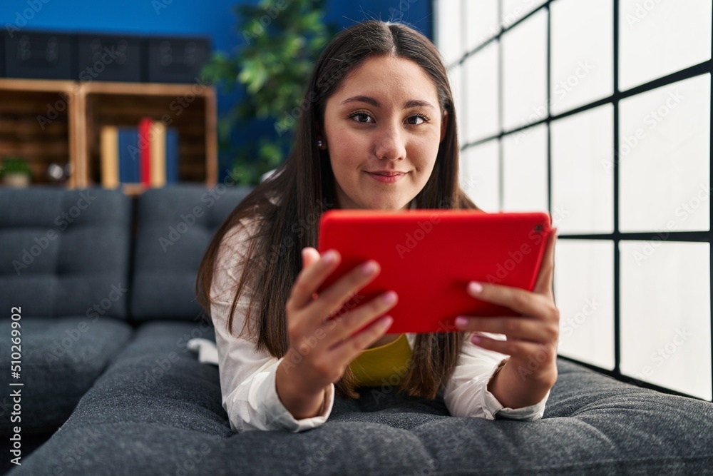 Young hispanic woman using touchpad lying on sofa at home Young hispanic woman using touchpad lying on sofa at home