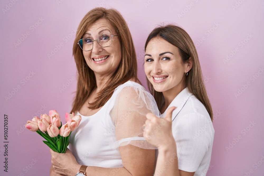 Hispanic mother and daughter holding pink tulips bouquet smiling happy and positive, thumb up doing excellent and approval sign Hispanic mother and daughter holding pink tulips bouquet smiling happy and positive, thumb up doing excellent and approval sign