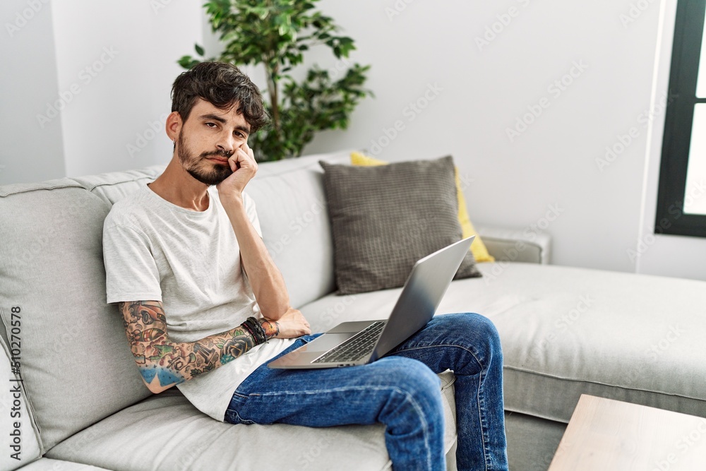 Hispanic man with beard sitting on the sofa thinking looking tired and bored with depression problems with crossed arms.