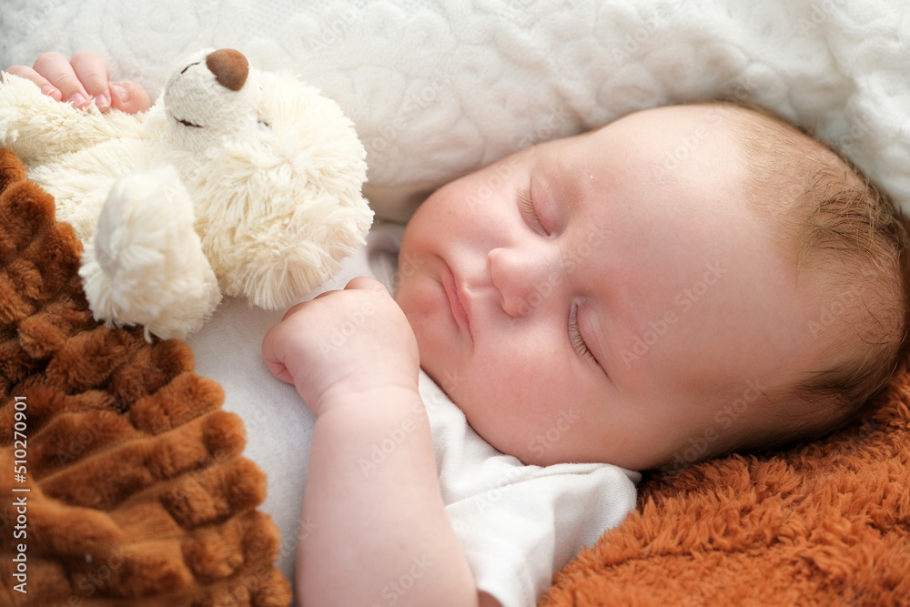 a newborn baby sleeps on a bed. A teddy bear lies nearby. mother and child. a newborn baby sleeps on a bed. A teddy bear lies nearby. mother and child.