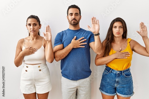 Group of young hispanic people standing over isolated background swearing with hand on chest and open palm  making a loyalty promise oath