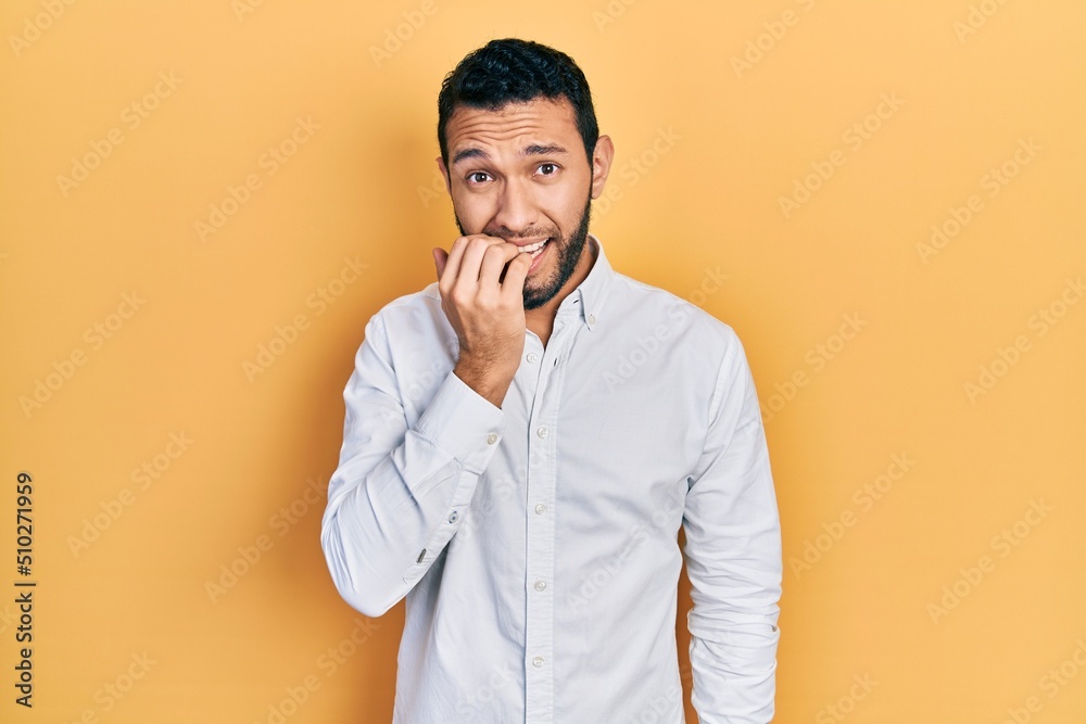 Hispanic man with beard wearing business shirt looking stressed and nervous with hands on mouth biting nails. anxiety problem. Hispanic man with beard wearing business shirt looking stressed and nervous with hands on mouth biting nails. anxiety problem.