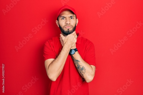 Hispanic man with beard wearing delivery uniform and cap shouting suffocate because painful strangle. health problem. asphyxiate and suicide concept.