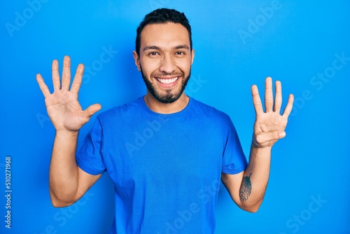 Hispanic man with beard wearing casual blue t shirt showing and pointing up with fingers number nine while smiling confident and happy.