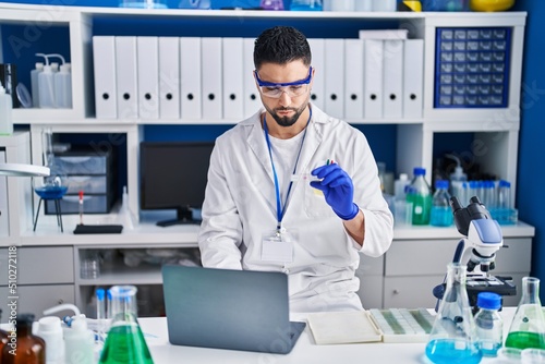 Young arab man scientist using laptop holding sample at laboratory
