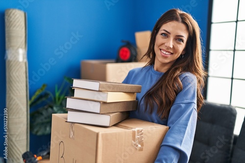 Young hispanic woman smiling confident holding books package at new home