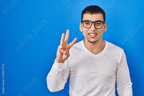 Young arab man wearing casual white shirt and glasses showing and pointing up with fingers number three while smiling confident and happy.