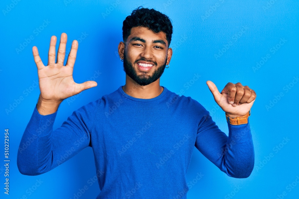 Arab man with beard wearing casual blue sweater showing and pointing up with fingers number six while smiling confident and happy.