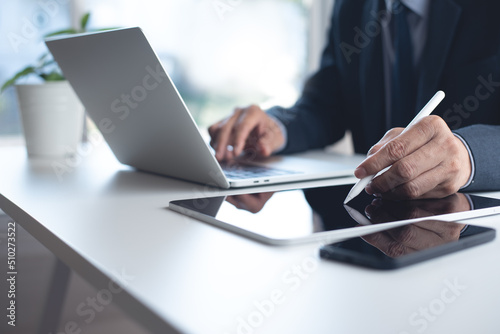 Closeup of businessman using stylus pen on digital tablet and working on laptop computer with mobile smart phone on office table