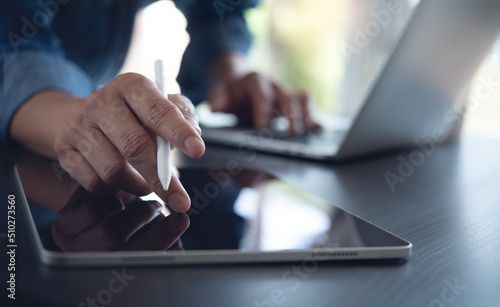 Close up of business man using digital tablet and working on laptop computer on office table