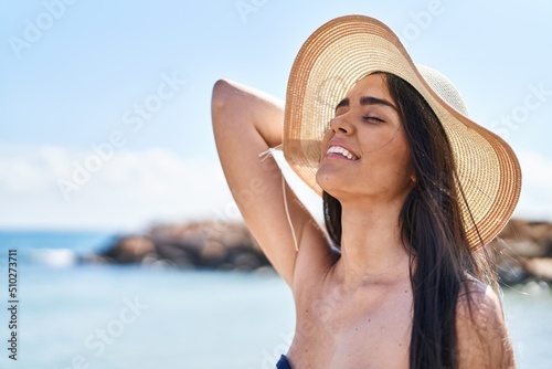 Young hispanic woman smiling confident wearing bikini and summer hat at seaside © Krakenimages.com