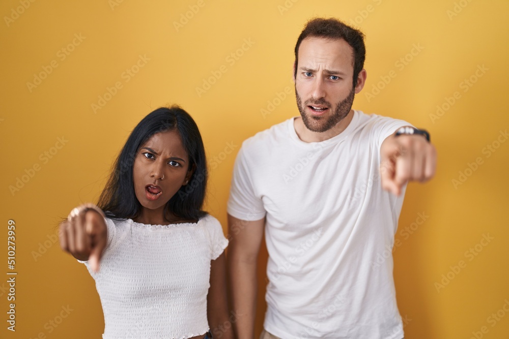 Interracial couple standing over yellow background pointing displeased and frustrated to the camera, angry and furious with you Interracial couple standing over yellow background pointing displeased and frustrated to the camera, angry and furious with you