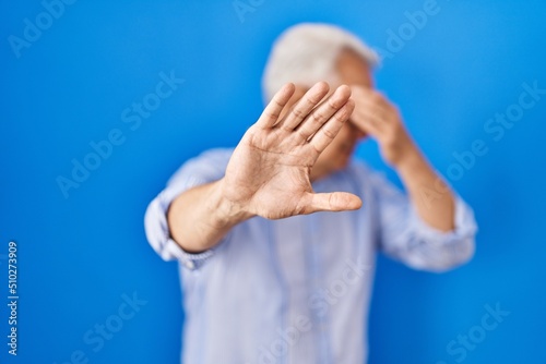 Hispanic senior man wearing glasses covering eyes with hands and doing stop gesture with sad and fear expression. embarrassed and negative concept.