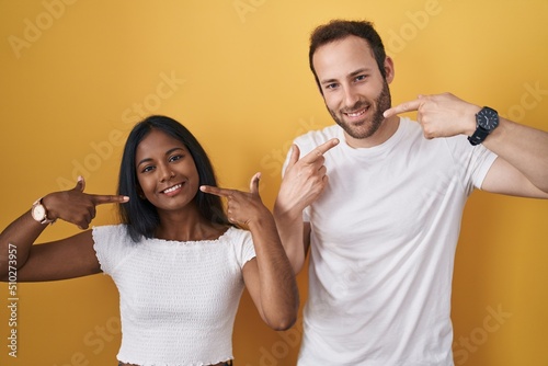 Interracial couple standing over yellow background smiling cheerful showing and pointing with fingers teeth and mouth. dental health concept.