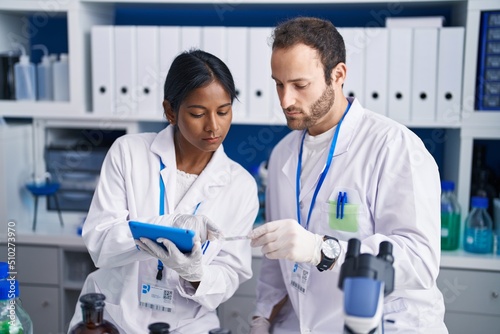 Man and woman scientists using touchpad holding sample at laboratory
