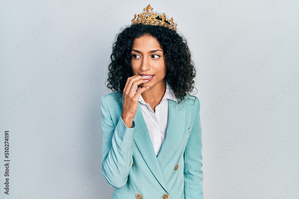 Young latin girl wearing business clothes and queen crown looking stressed and nervous with hands on mouth biting nails. anxiety problem. Young latin girl wearing business clothes and queen crown looking stressed and nervous with hands on mouth biting nails. anxiety problem.
