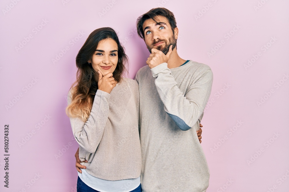 Young hispanic couple wearing casual clothes with hand on chin thinking about question, pensive expression. smiling and thoughtful face. doubt concept. Young hispanic couple wearing casual clothes with hand on chin thinking about question, pensive expression. smiling and thoughtful face. doubt concept.