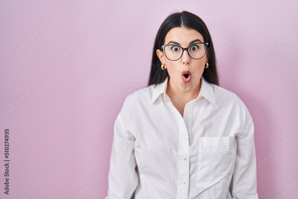 Young brunette woman standing over pink background afraid and shocked with surprise expression, fear and excited face.