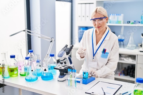 Young blonde woman wearing scientist uniform measuring liquid at laboratory