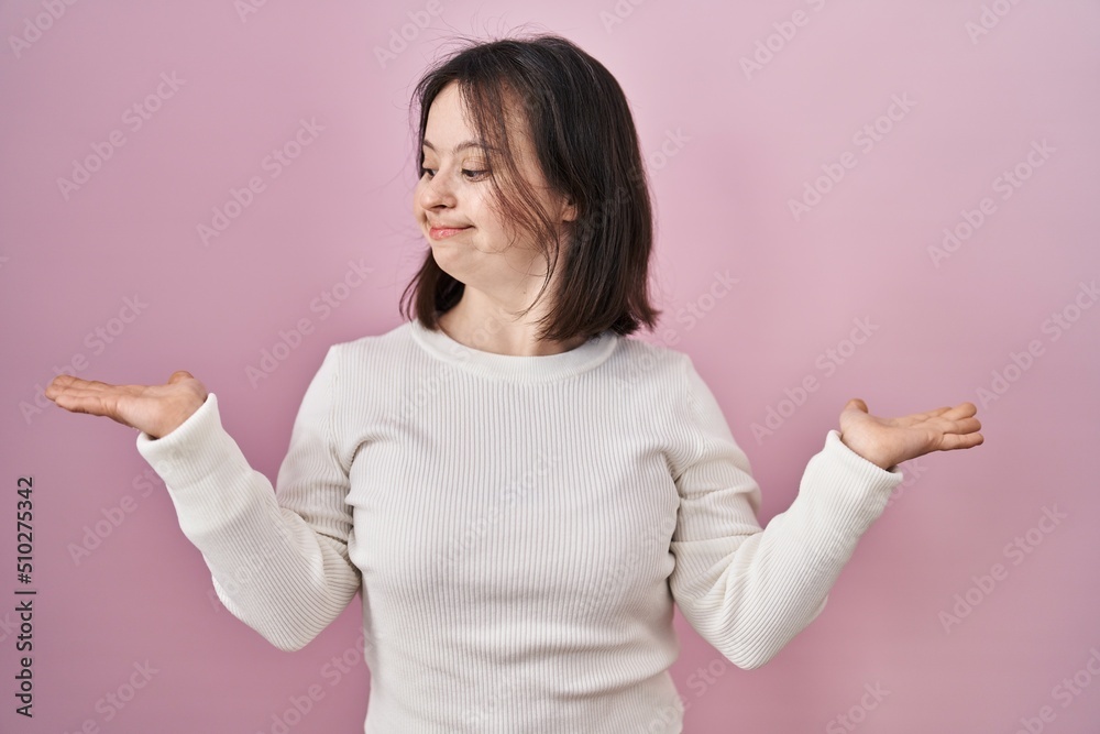 Woman with down syndrome standing over pink background smiling showing both hands open palms, presenting and advertising comparison and balance Woman with down syndrome standing over pink background smiling showing both hands open palms, presenting and advertising comparison and balance