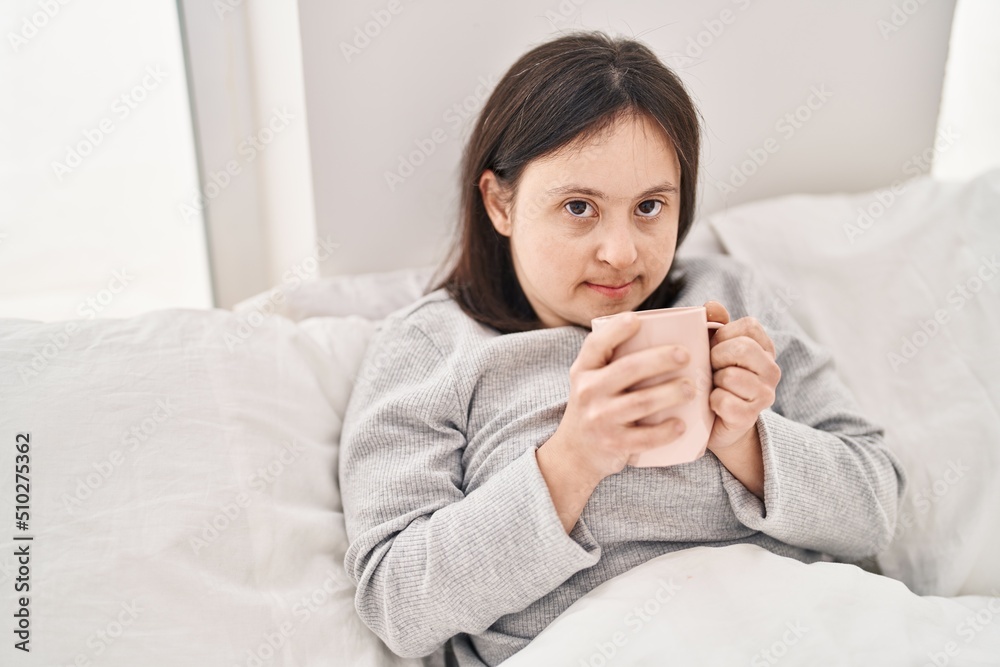 Young woman with down syndrome drinking cup of coffee sitting on bed at bedroom Young woman with down syndrome drinking cup of coffee sitting on bed at bedroom