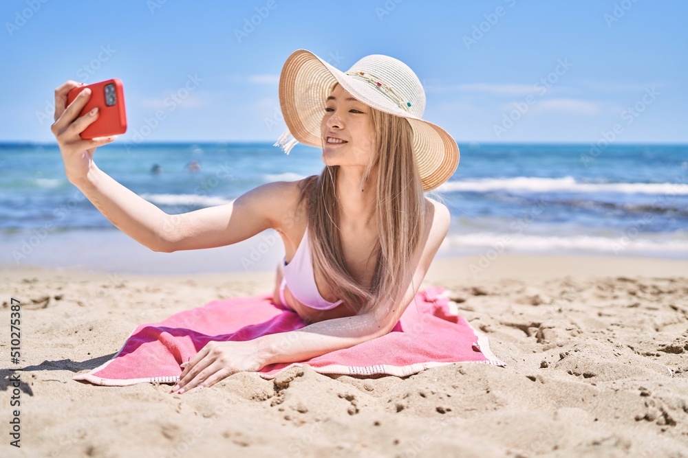 Young chinese girl wearing bikini make selfie by the smartphone at the beach. Young chinese girl wearing bikini make selfie by the smartphone at the beach.