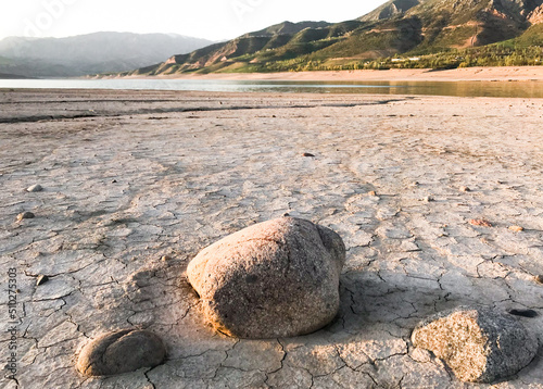 Beautiful landscape with setting sun: mountains, lake, cracked earth with stones -dried-up riverbend photo