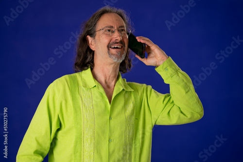 Promoter mature man in green guayabera shirt talking on mobile cell phone with excitement for promo commercial area isolated on solid purple background studio photo