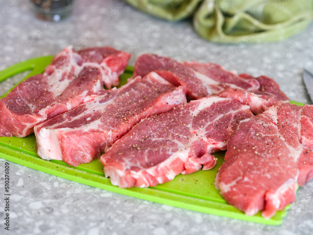 Peppered and salted raw pork slices on a green cutting board