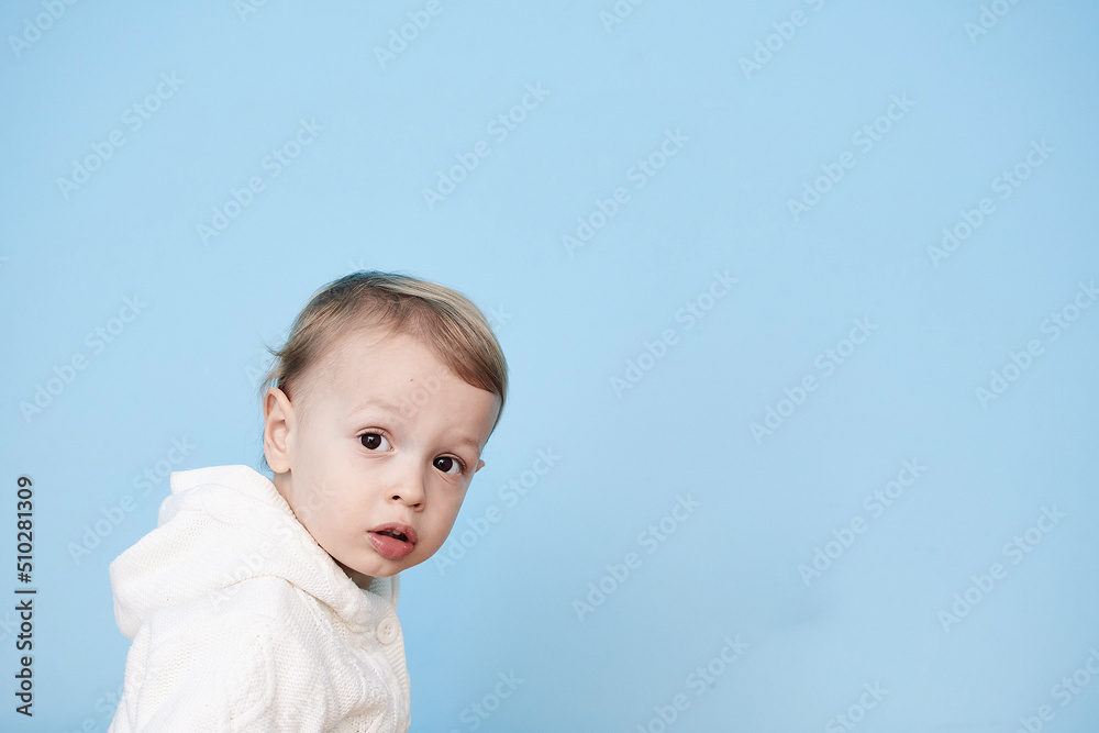 a little boy of 2 years sits in a white jacket on a blue background and thinks laughs happy sad sadness cheerful advertisement for children a little boy of 2 years sits in a white jacket on a blue background and thinks laughs happy sad sadness cheerful advertisement for children