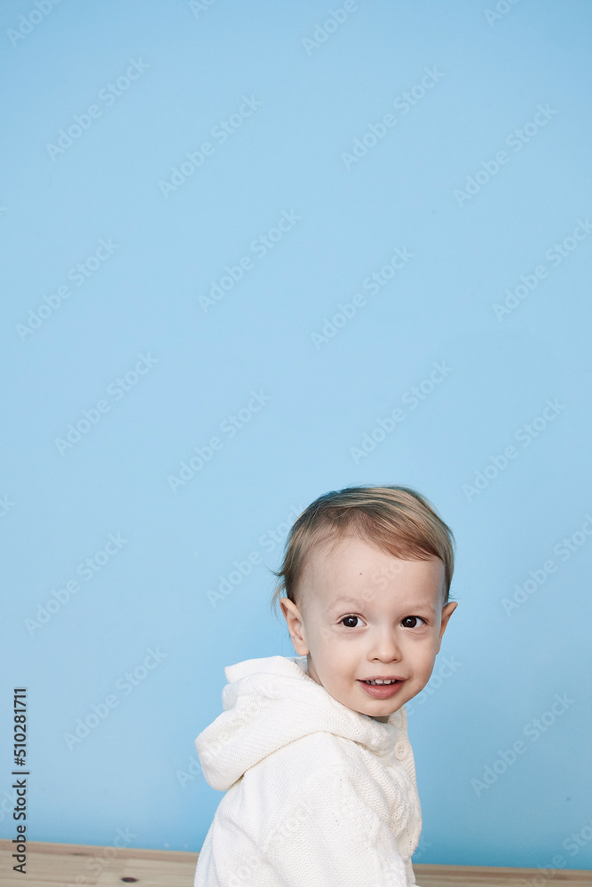 a little boy of 2 years sits in a white jacket on a blue background and thinks laughs happy sad sadness cheerful advertisement for children a little boy of 2 years sits in a white jacket on a blue background and thinks laughs happy sad sadness cheerful advertisement for children