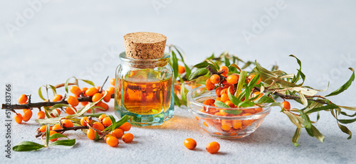 Glass bottle with sea buckthorn oil, berries and branches of sea buckthorn on light background photo