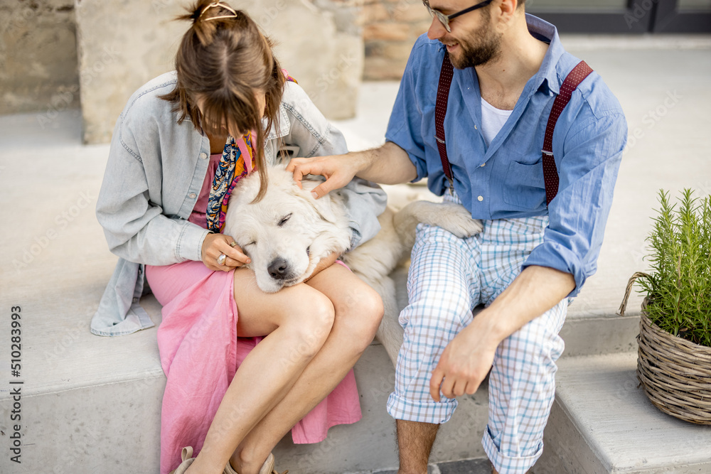 Stylish couple have fun and sit with their dog on a street Stylish couple have fun and sit with their dog on a street
