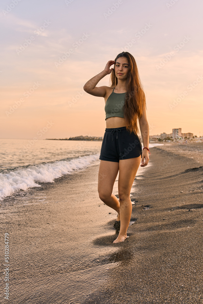 portrait of a young spanish tanned woman walking along the seashore at the beach on the sunset