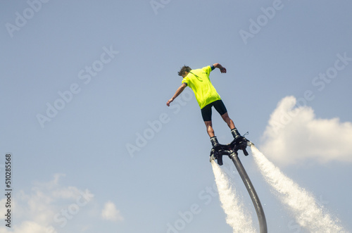 aquatic aviation, flyboarding, man in the green shirt flies on flyboard in the blue sky