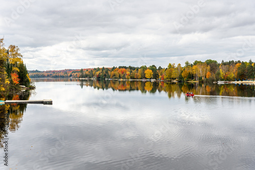 Beautiful lake with forested shores at the peak of fall foliage on a cloudy autumn day. People on a canoe are visible in the midlle of the lake. Ontario, Canada. photo