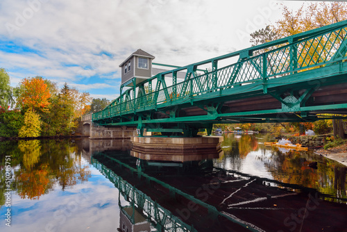 Swing bridge across a river on a partly cloudy autumn day. Colourful autumn trees reflecting in water.