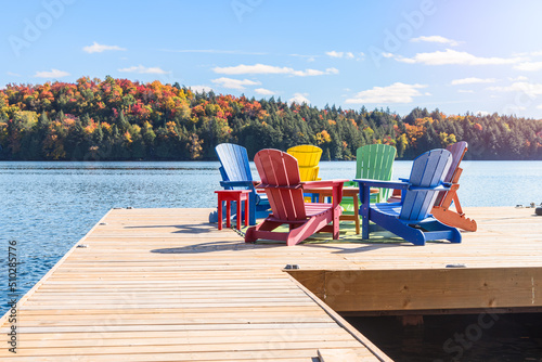 Colourful adirondack chairs around atable on a wooden pier on a lake on a sunny autumn day. photo